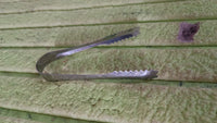 Stainless steel tongs resting on a rustic wooden surface, highlighting versatility.